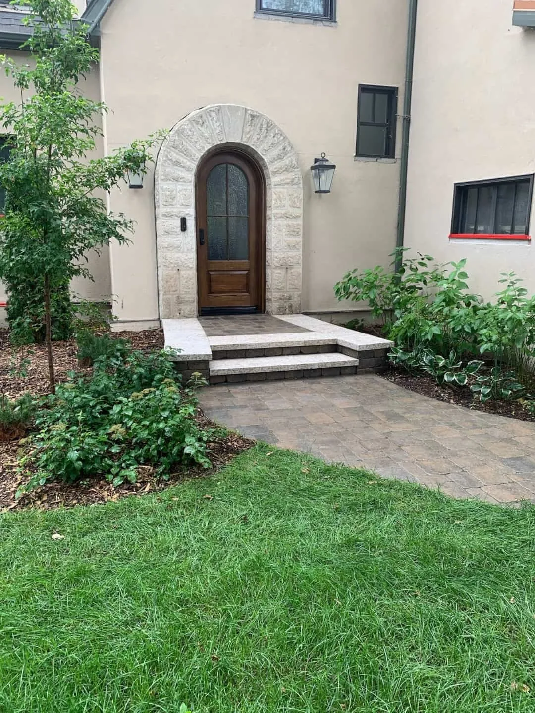 Tumbled paver walkway and stone steps leading to an arched stone entry
