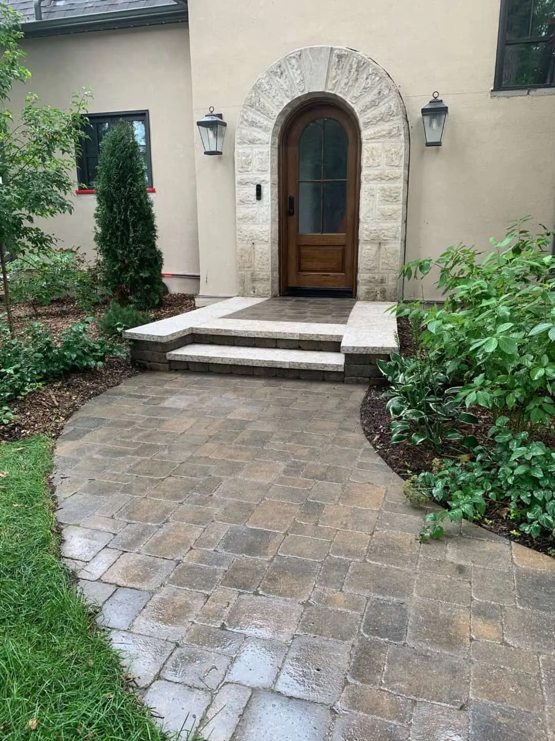 Paver walkway and stone steps at an arched front entry