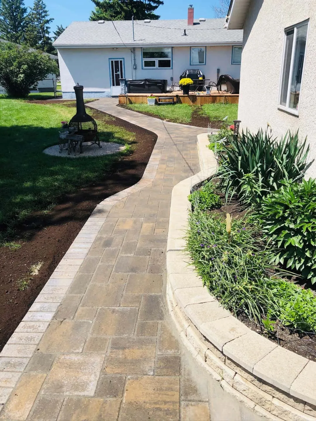 Curved paver walkway with a charcoal soldier-course border running past a block retaining wall and planting bed