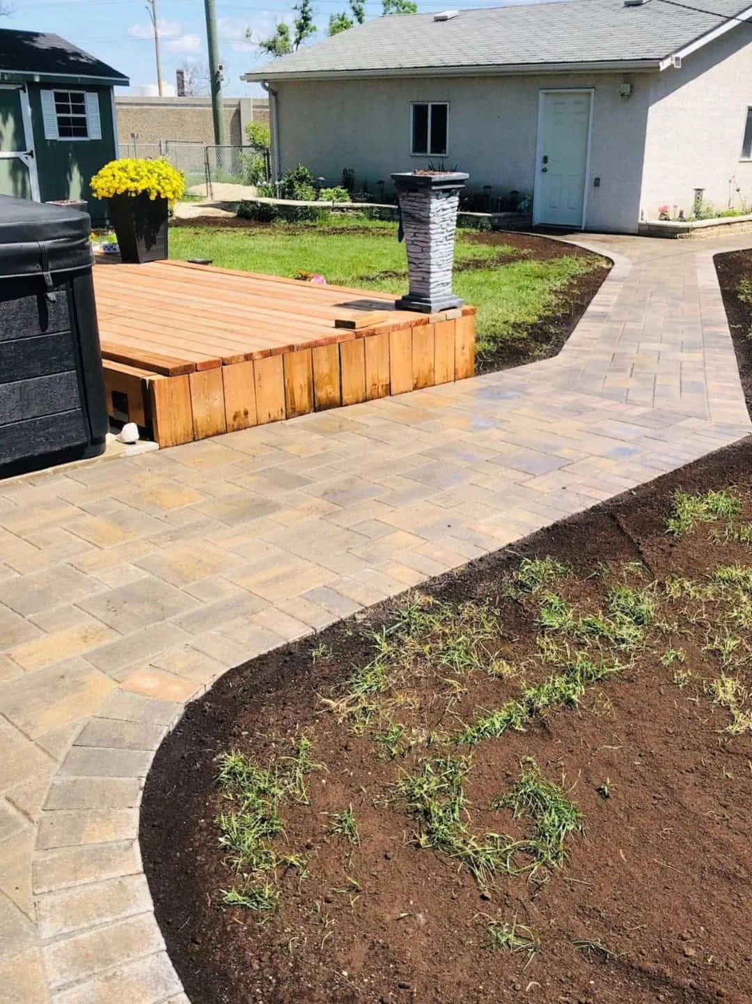 Paver walkway leaving a cedar deck and hot tub and curving toward the back door of a bungalow
