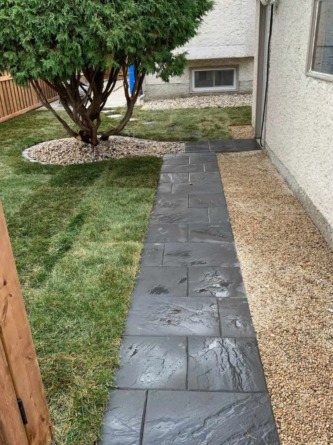 Charcoal slate-textured paver walkway running between new sod and a gravel strip along a stucco house