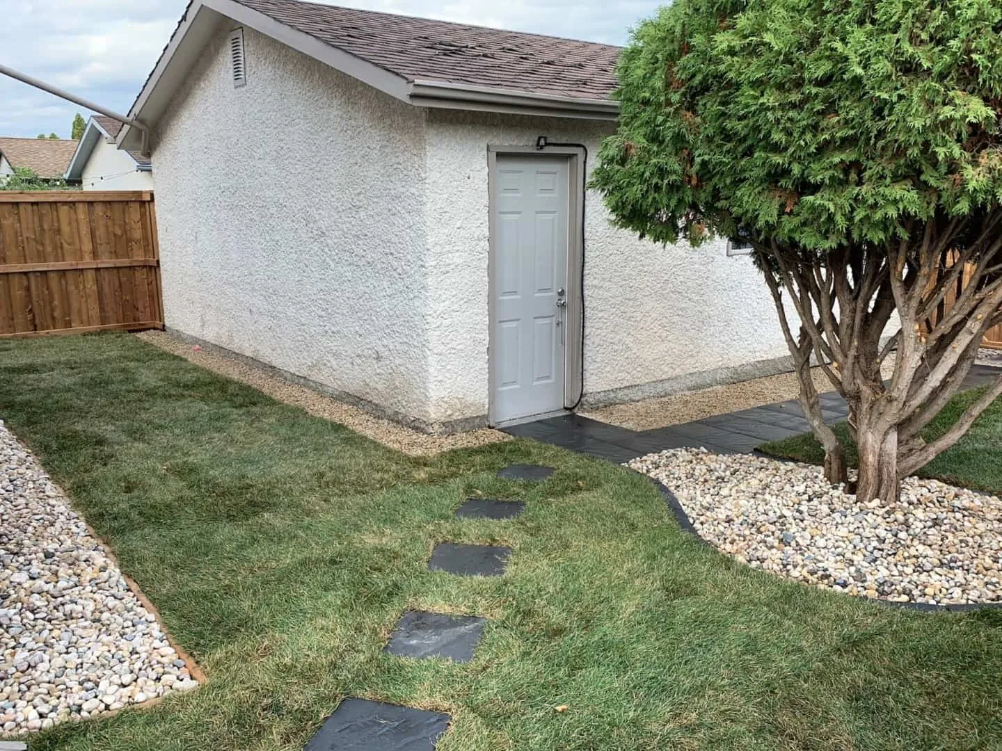 New sod laid around a garage with white river rock beds, black edging and slate stepping stones