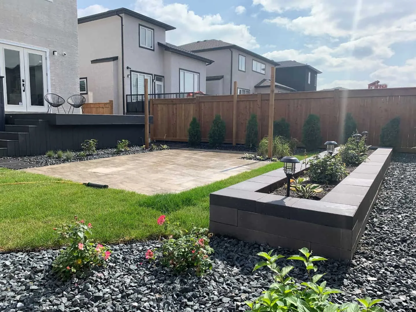 Charcoal block raised planter, paver patio and black rock beds in a new back yard