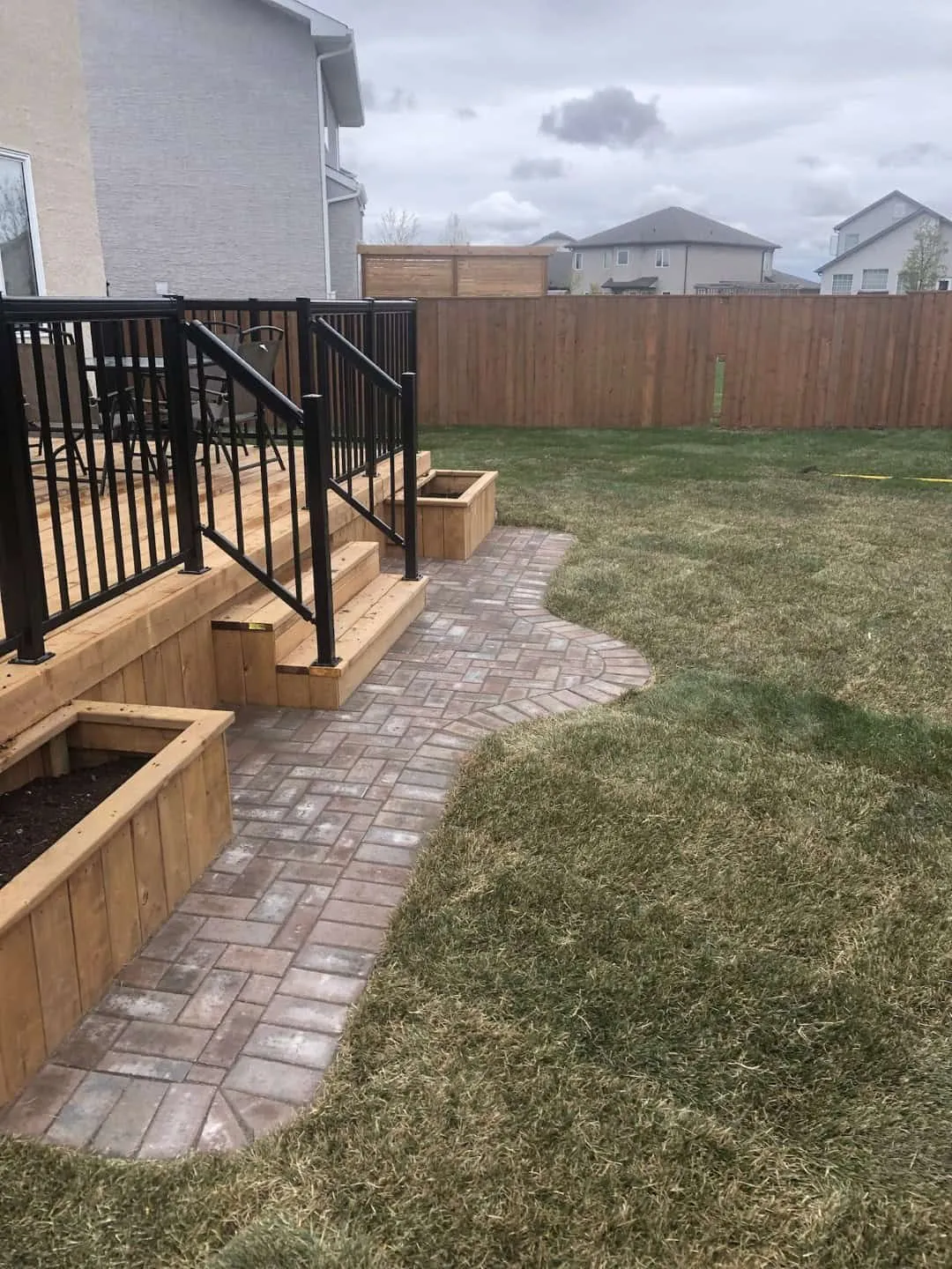 Brick-pattern paver walkway curving out from the steps of a cedar deck along the edge of a new lawn