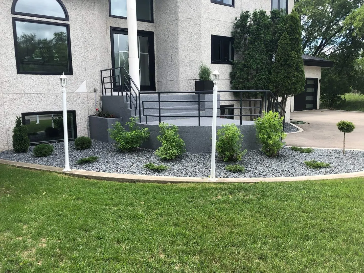 Aggregate steps and a black rock planting bed across a front yard