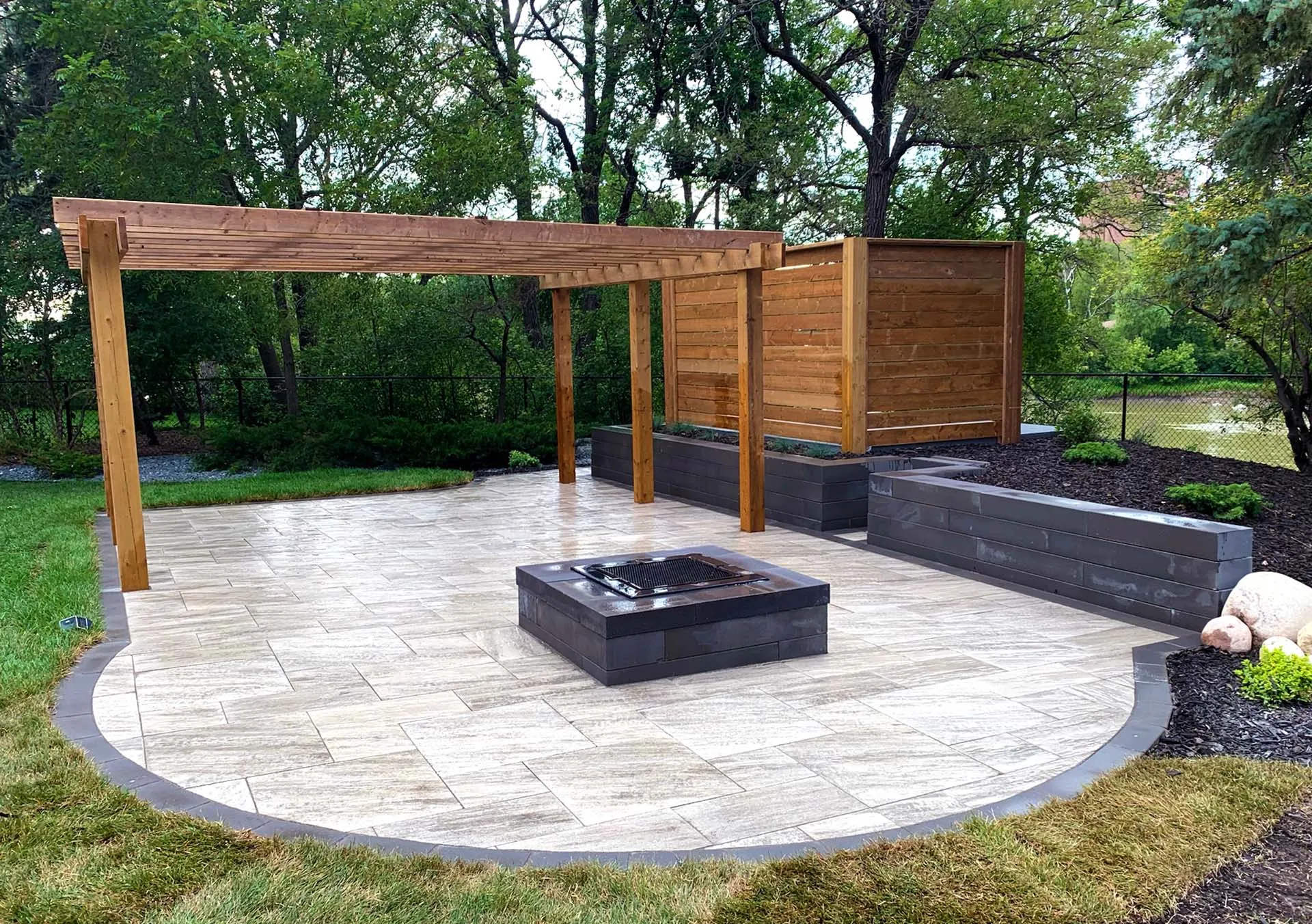 Cedar pergola over a curved travertine paver patio with a charcoal block fire pit